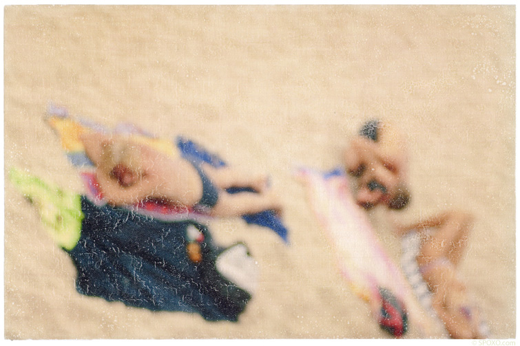 Foto-Mischtechnik von SPOXO -Eine Frage der Perspektive- Zwei Sonnenanbeter von oben, eingebettet in hellen Sand, bunte Handtücher, entspannte Körper, kein Horizont, keine Orientierung.
