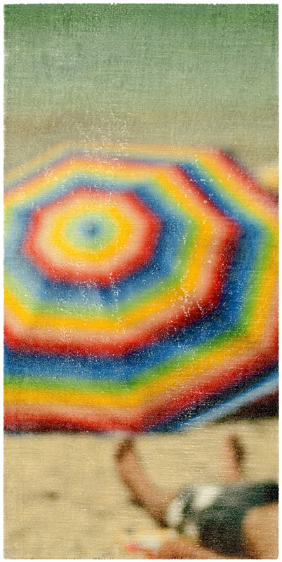 Foto-Mischtechnik von SPOXO -Ein irrer Tripp- Ein leuchtend bunter Sonnenschirm in Rot, Gelb und Blau füllt fast das gesamte Hochformat, darunter ein Hauch Sand, und eine Andeutung von Mensch.