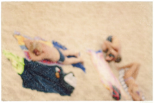Foto-Mischtechnik von SPOXO -Eine Frage der Perspektive- Zwei Sonnenanbeter von oben, eingebettet in hellen Sand, bunte Handtücher, entspannte Körper, kein Horizont, keine Orientierung.